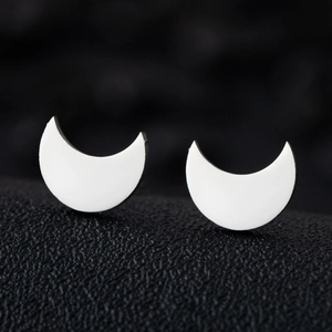 Macro view of polished silver crescent moon stud earrings on a textured black background