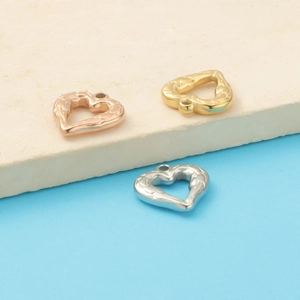 Three hollow heart-shaped metal charms in gold, silver, and rose gold on a stone base