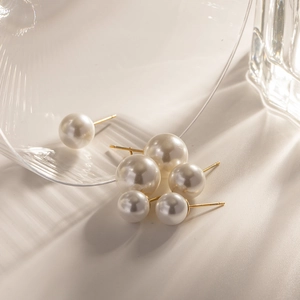 Detailed view of three pairs of gradient faux pearl stud earrings with gold pins