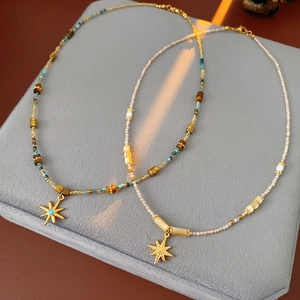 Detail of beaded starburst necklaces with gold pendants on a soft grey velvet base