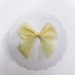 Close-up of a light yellow polka dot organza bow hair accessory on white cardstock