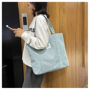 Detail view of mint green corduroy tote bag worn over the shoulder by a model