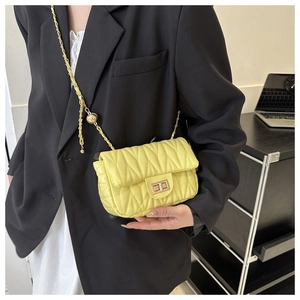Close-up of quilted yellow leather crossbody bag with gold chain strap on black blazer