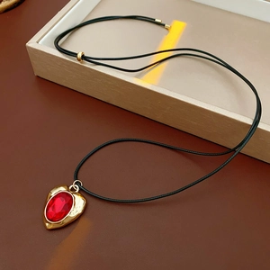 Detailed close-up of a vintage heart pendant with red crystal on a black cord necklace