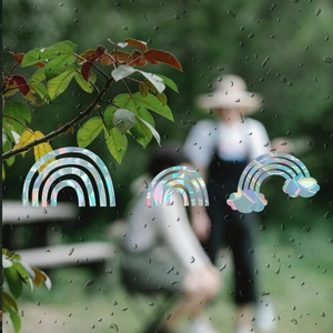 Close-up of holographic rainbow cloud prism window stickers on wet glass surface