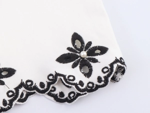 Detailed view of white dress featuring black wavy embroidery and a pearl accent