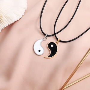 Close-up of black and white Yin Yang couple necklaces on soft pink silk background