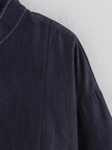 Detailed close-up of dark blue denim jacket shoulder with white contrast stitching accents