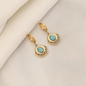 Detailed shot of retro gold hollow earrings with turquoise stone on white fabric