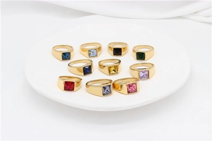 Close-up of ten gold signet rings with colorful square gemstones on a white ceramic plate