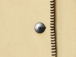 Detail of wool blend jacket featuring black buttons and brown contrast stitching