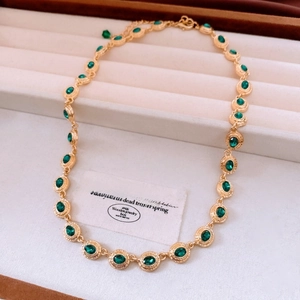 Detailed view of vintage gold necklace with oval green stones and pleated textured bezels