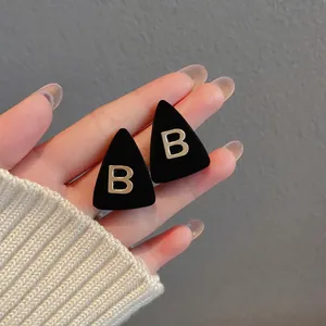 Detail of triangle earring with black velvet texture and golden letter B metal accent