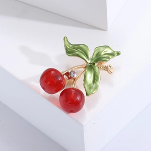Broche cerise en émail rouge avec tige dorée et strass sur présentoir blanc