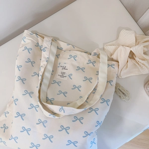 Close-up of canvas tote bag featuring light blue bow prints and central fabric label