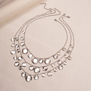 Detail of a three-layer silver necklace with hammered coin pendants on a beige background