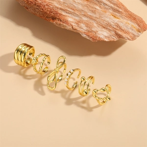 Set of 6 gold ear cuffs with minimalist knot, butterfly, and pearl designs on beige backdrop