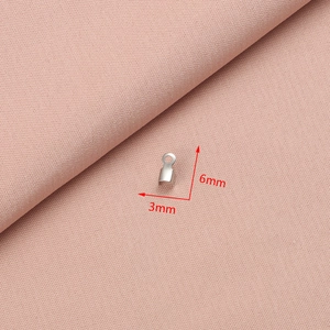 Detailed view of silver stainless steel cord ends with 3mm x 6mm dimensions on pink cloth