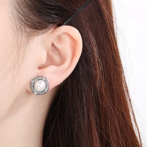 Close-up of elegant silver halo pearl stud earrings with sparkling zircon on model's ear