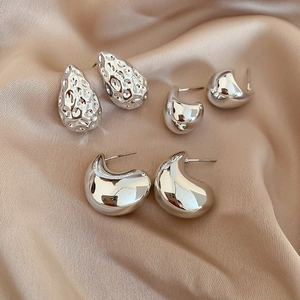Close-up of three silver geometric teardrop earrings on elegant champagne silk fabric
