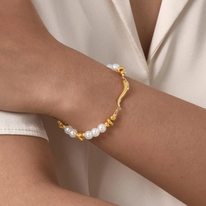 Detail of a gold stainless steel bracelet featuring faux pearls and a smiley face charm