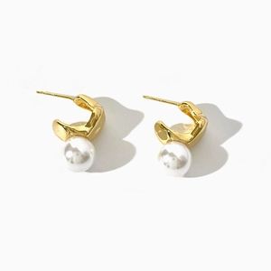 Boucles d'oreilles dorées irrégulières en métal avec perles blanches sur fond blanc pur