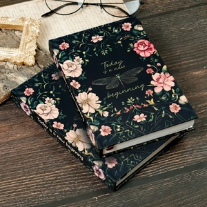 Retro hardcover notebook with floral and dragonfly art on a vintage wood background