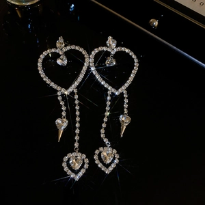Macro detail of silver heart tassel earrings with sparkling rhinestones on black background