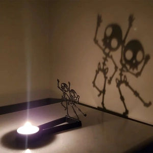 Macro shot of metal candle holder projecting dancing skeleton shadows on beige wall