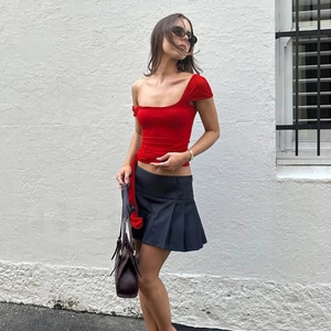 Detail view of a red one-shoulder top paired with a black pleated skirt in street style