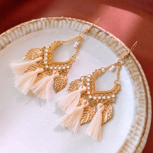 Detail of bohemian gold leaf earrings with cream cotton tassels on ceramic tray