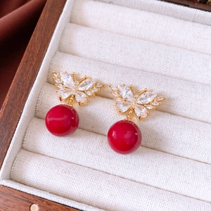 Macro view of gold butterfly earrings with red spherical charms and zircon inlays