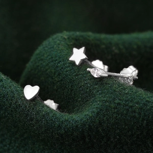 Macro shot of silver heart and star earrings set with marquise zircon on green velvet