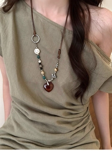 Detail of vintage beaded necklace with heart pendant on brown cord and green top