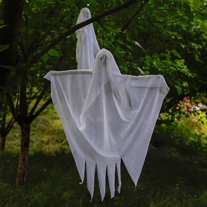 Hanging Halloween white ghost decoration with spooky face on a tree branch outdoors