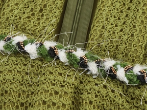 Detail of green knit dress featuring colorful woven trim and delicate gold beads