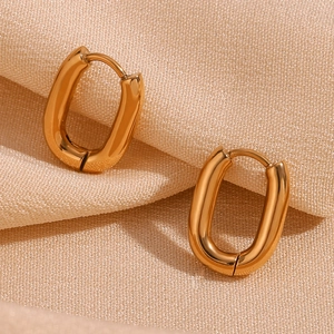 Close-up of gold oval hoop earrings with smooth metallic finish on beige fabric