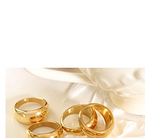 Close-up of four minimalist polished gold band rings scattered on a white surface
