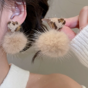 Close-up of beige plush pompom earrings with leopard print details worn on a model