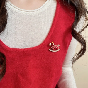 Detail of red enamel rocking horse brooch with zircon inlay on red knit vest clothing