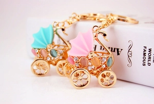 Close-up of golden rhinestone swan stroller keychains in pink and blue on a white book