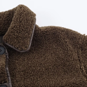 Detail of brown shearling jacket featuring faux leather piping and black button closure