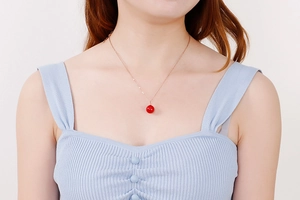 Détail d'une chaîne élégante en or rose avec un pendentif perle rouge sur un mannequin