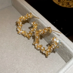 Macro shot of gold C-shaped earrings with shimmering crystals on grey velvet