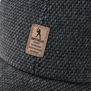 Close-up of knit texture and brown leather logo patch on dark gray winter baseball cap