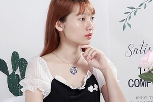 Close-up of a silver heart necklace with blue gemstone and LOVE engraving on a model