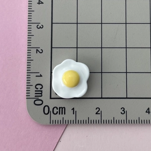 Macro detail of a 1.5cm fried egg resin charm on a grid mat for DIY crafts