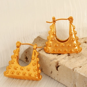 Golden padlock earrings with textured dot pattern on a minimalist stone background