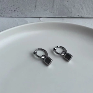 Detailed close-up of a silver hoop earring featuring a minimalist metal cube pendant