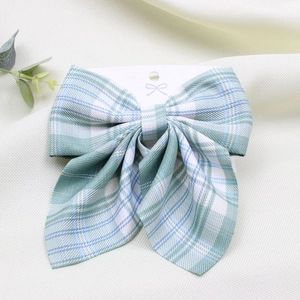 Detail of green and white plaid bow hair clip on cardstock with elegant fabric background